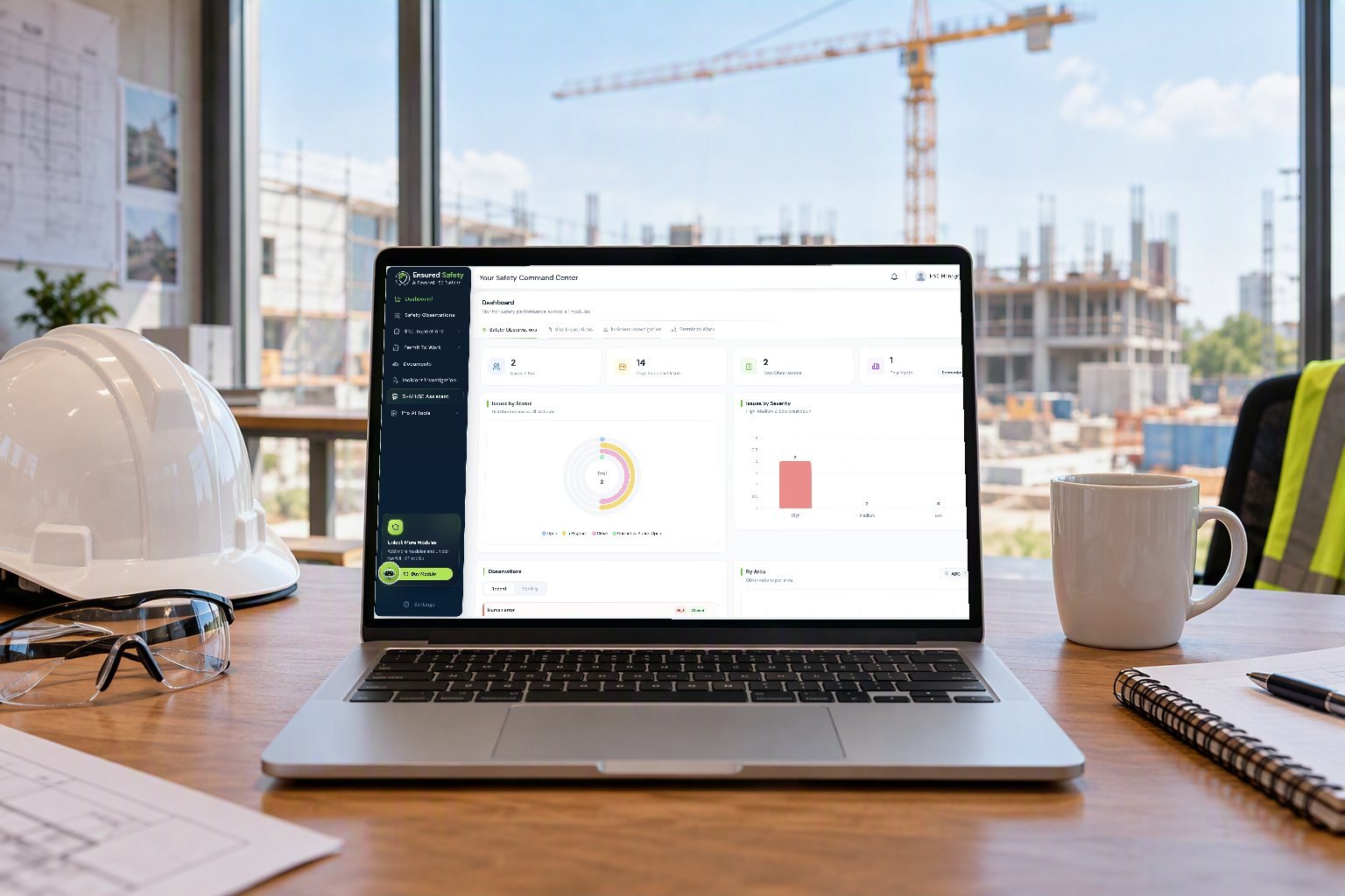 Laptop on a site-office desk showing the Ensured Safety dashboard, with a hard hat and safety glasses beside it